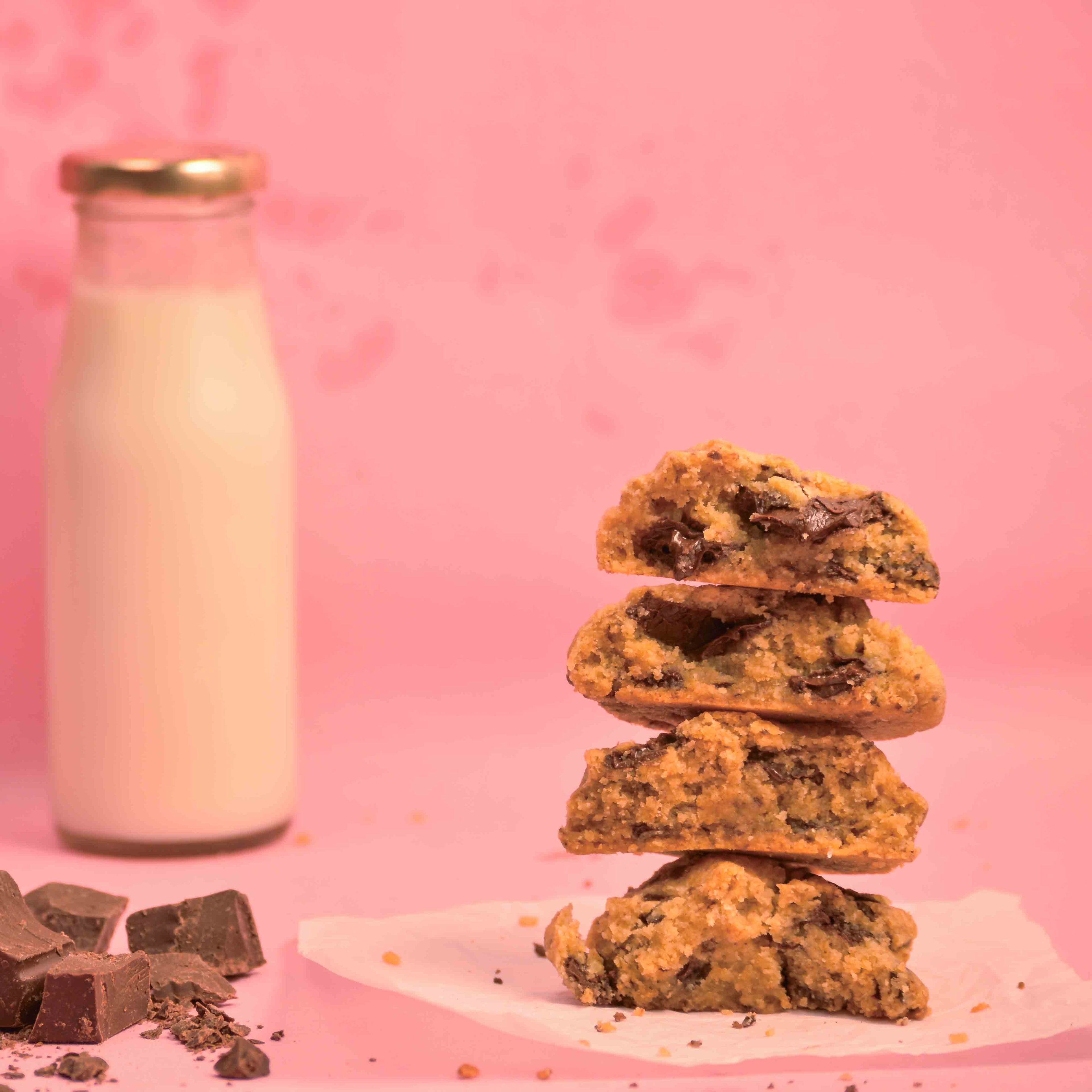 Stack of freshly baked American Choco chunk chip cookies with visible melted chocolate and milk bottle in the background with pink background product photography