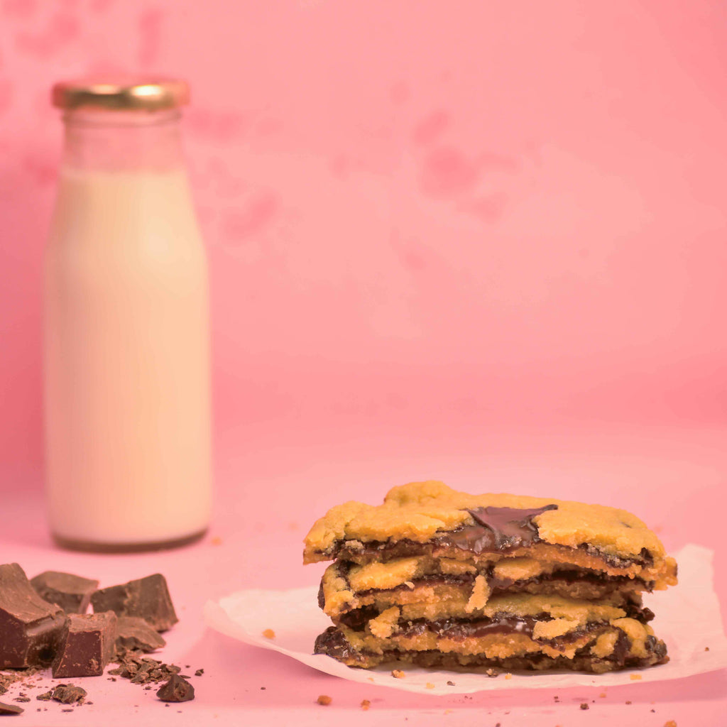 Stack of freshly baked Center filled chocolava cookies with visible melted chocolate and milk bottle in the background with pink background product photography