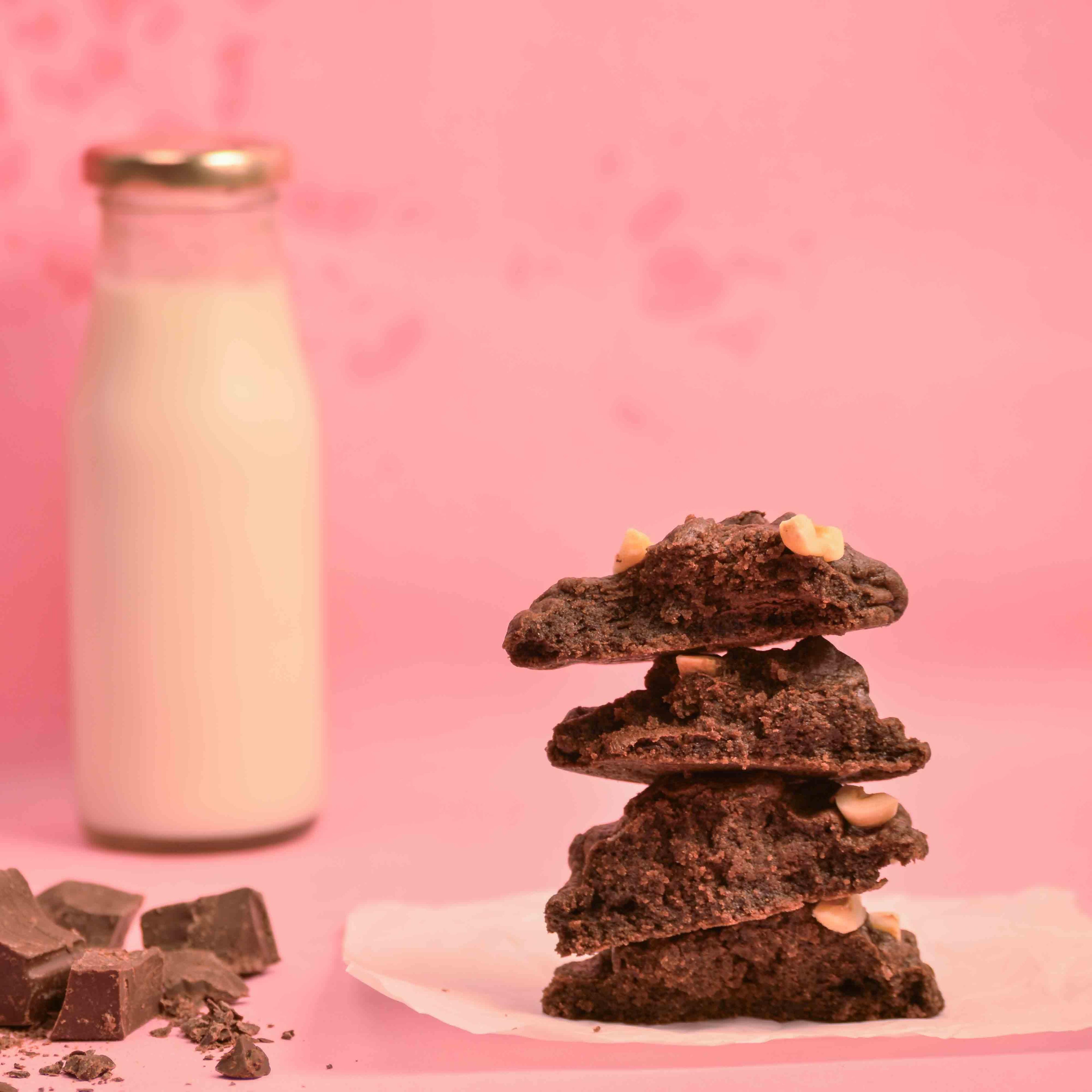 Stack of freshly baked Hazelnut chocolate chip cookies with visible melted chocolate and milk bottle in the background with pink background product photography
