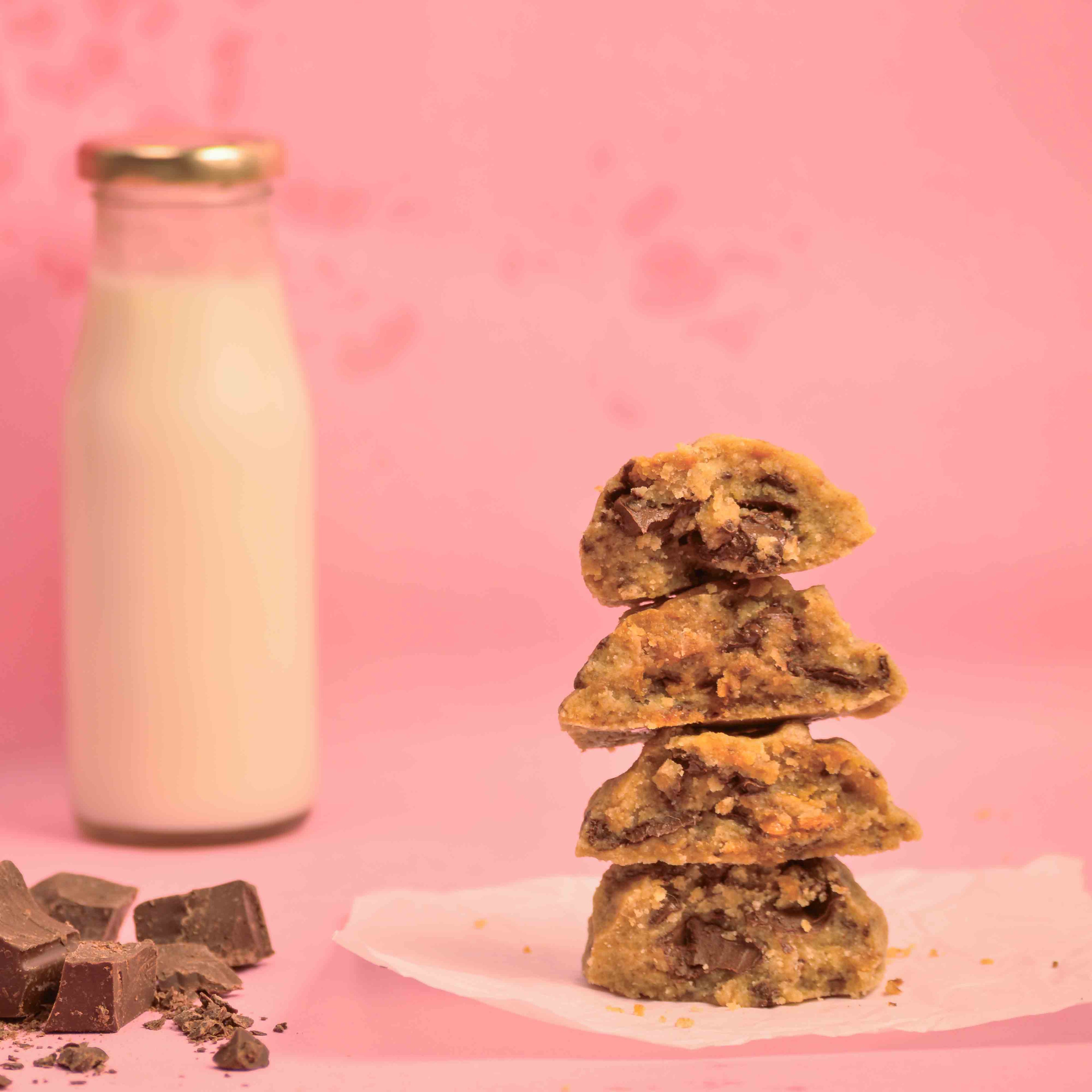 Stack of freshly baked NYC Choco Chunk cookies with visible melted chocolate and milk bottle in the background with pink background product photography