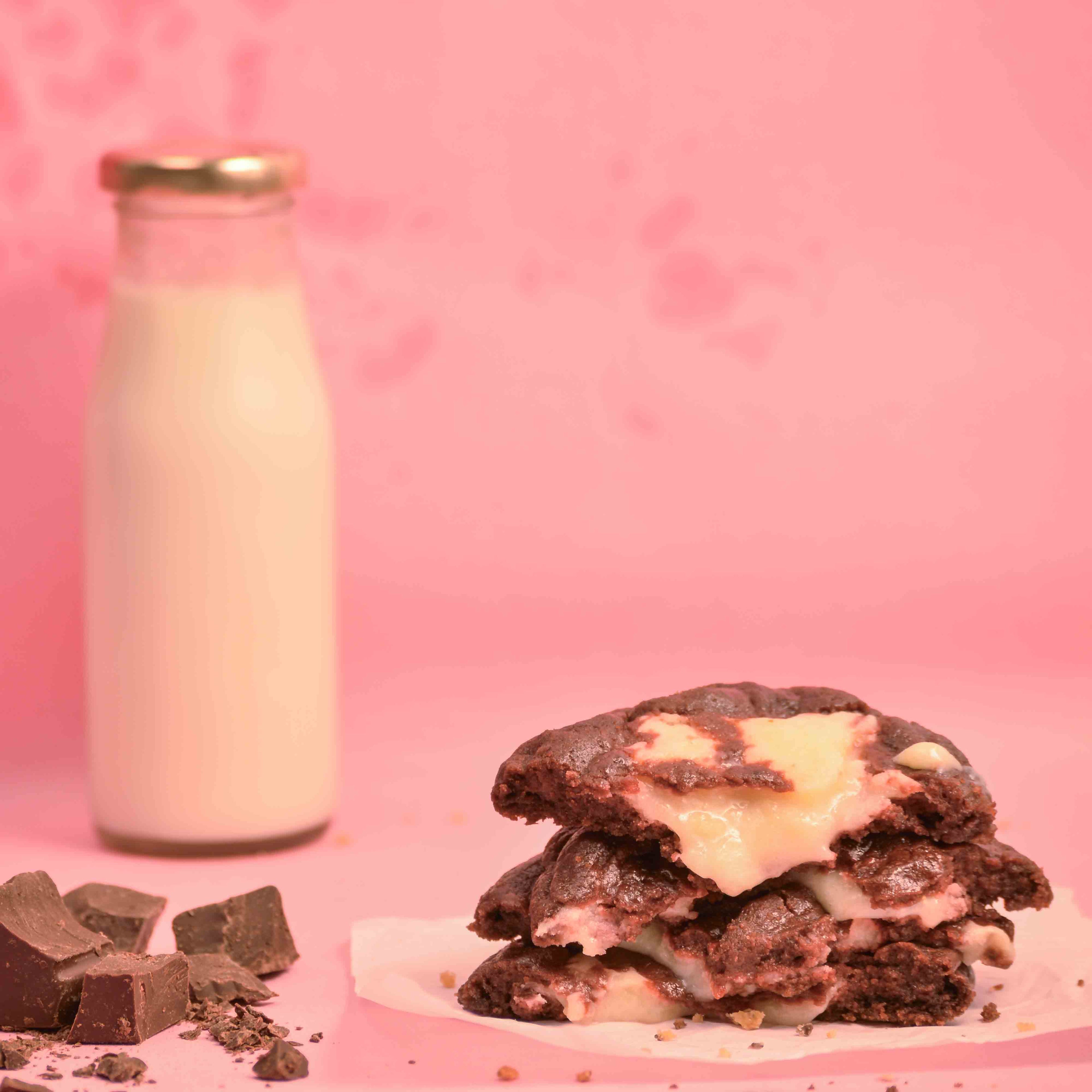 Stack of freshly baked Red velvet center filled cream cheese filling cookies with visible melted filling and milk bottle in the background with pink background product photography