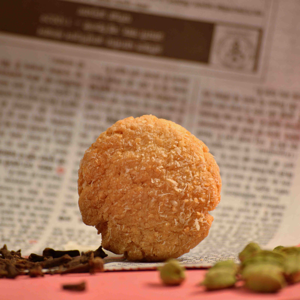 Coconut biscuit cookies crispy texture covered in coconut with newspaper as background and cardamon pods scattered professional product photography