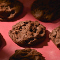 Thick Double chocolate cookies topped with sea salt gooey center and crispy edges on a pink background professional photography