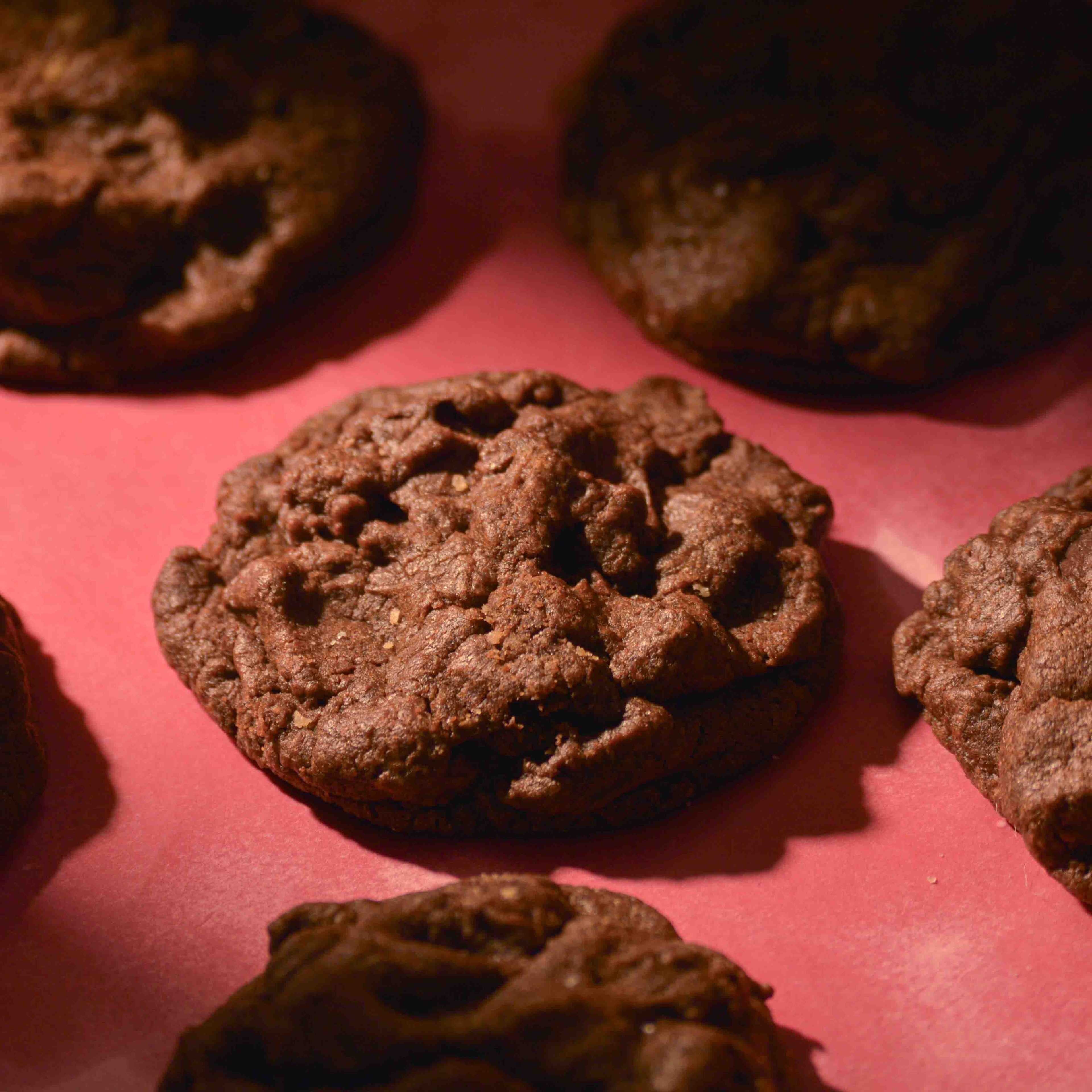 Thick Double chocolate cookies topped with sea salt gooey center and crispy edges on a pink background professional photography