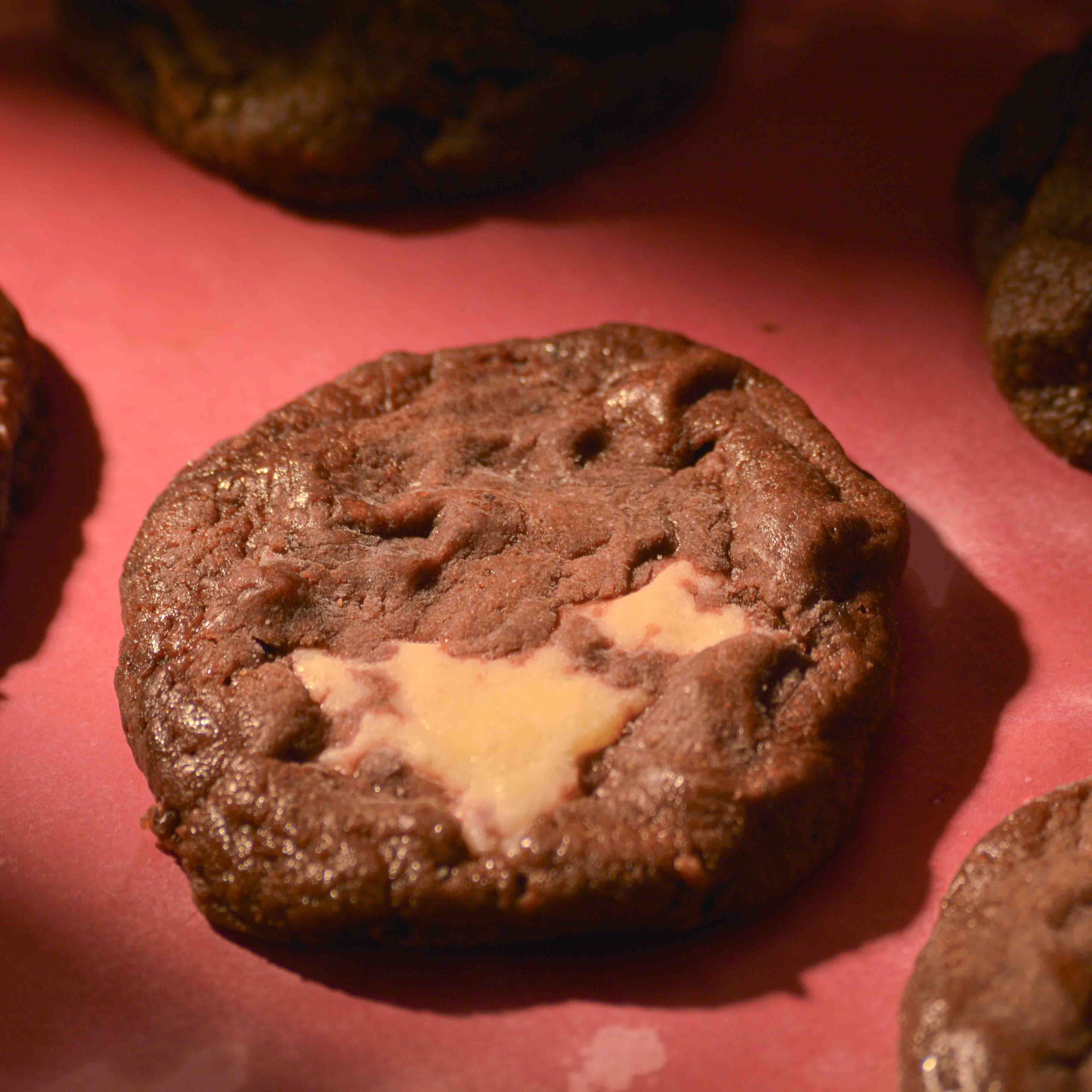 Thick Red velvet cream cheese filled cookies topped with sea salt gooey center and crispy edges on a pink background professional photography
